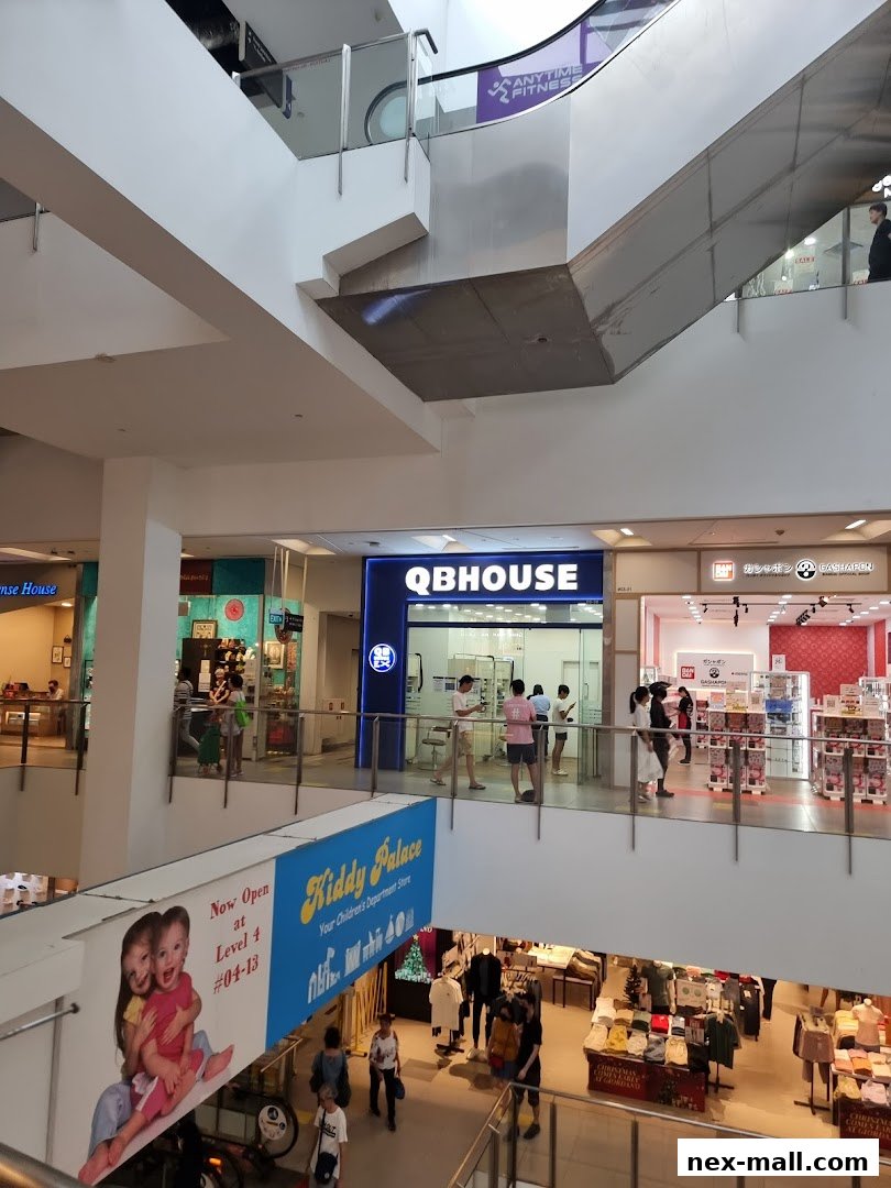 A view of the QB HOUSE store and other shops in a mall, with escalators and shoppers visible.