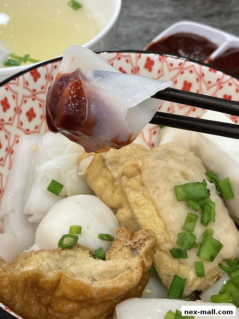 A close-up of a delicious dish with rice noodle rolls, fish balls, and fried tofu, garnished with scallions.