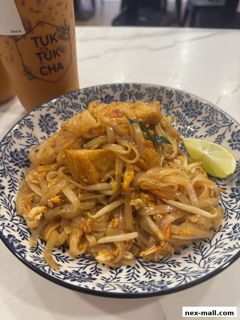 A plate of Pad Thai noodles with a lime wedge and two iced Thai milk teas.