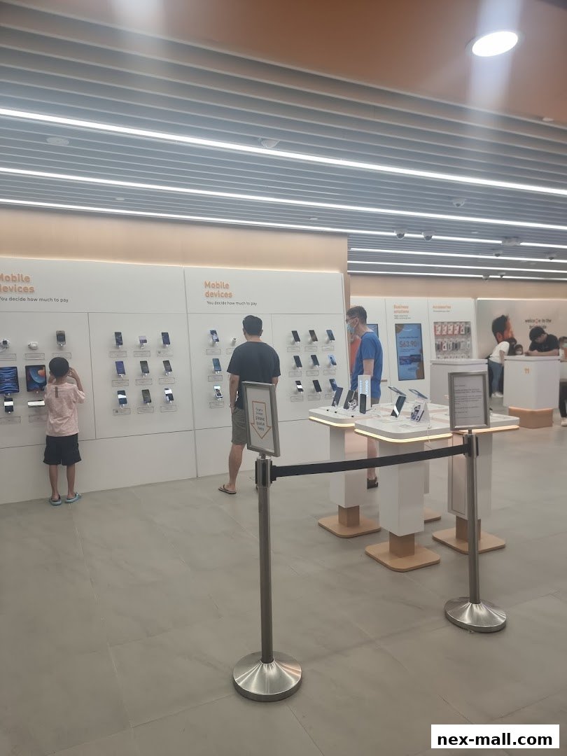 Customers browse mobile devices displayed on shelves and tables in a modern phone shop.