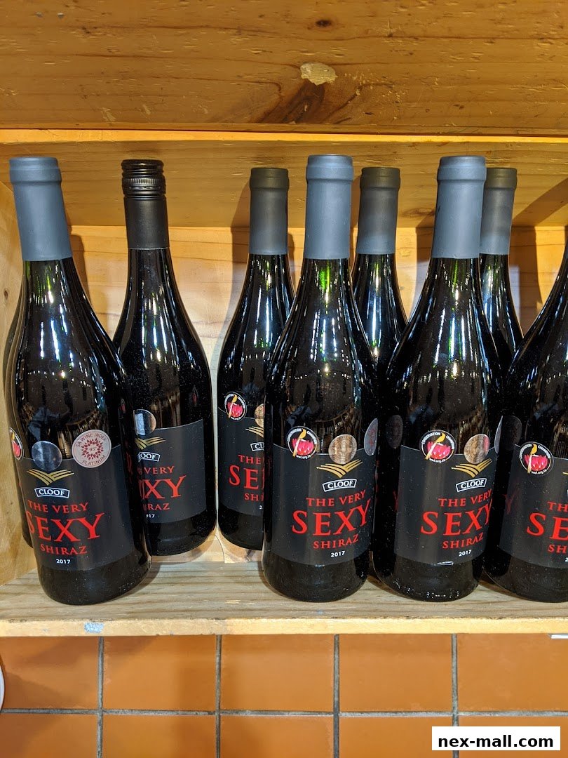 Several bottles of red wine, specifically 'The Very Sexy Shiraz', are neatly arranged on wooden shelves.