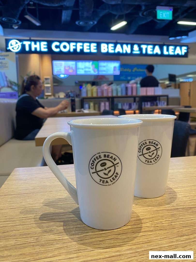 Two white mugs with The Coffee Bean & Tea Leaf logo sit on a wooden table.