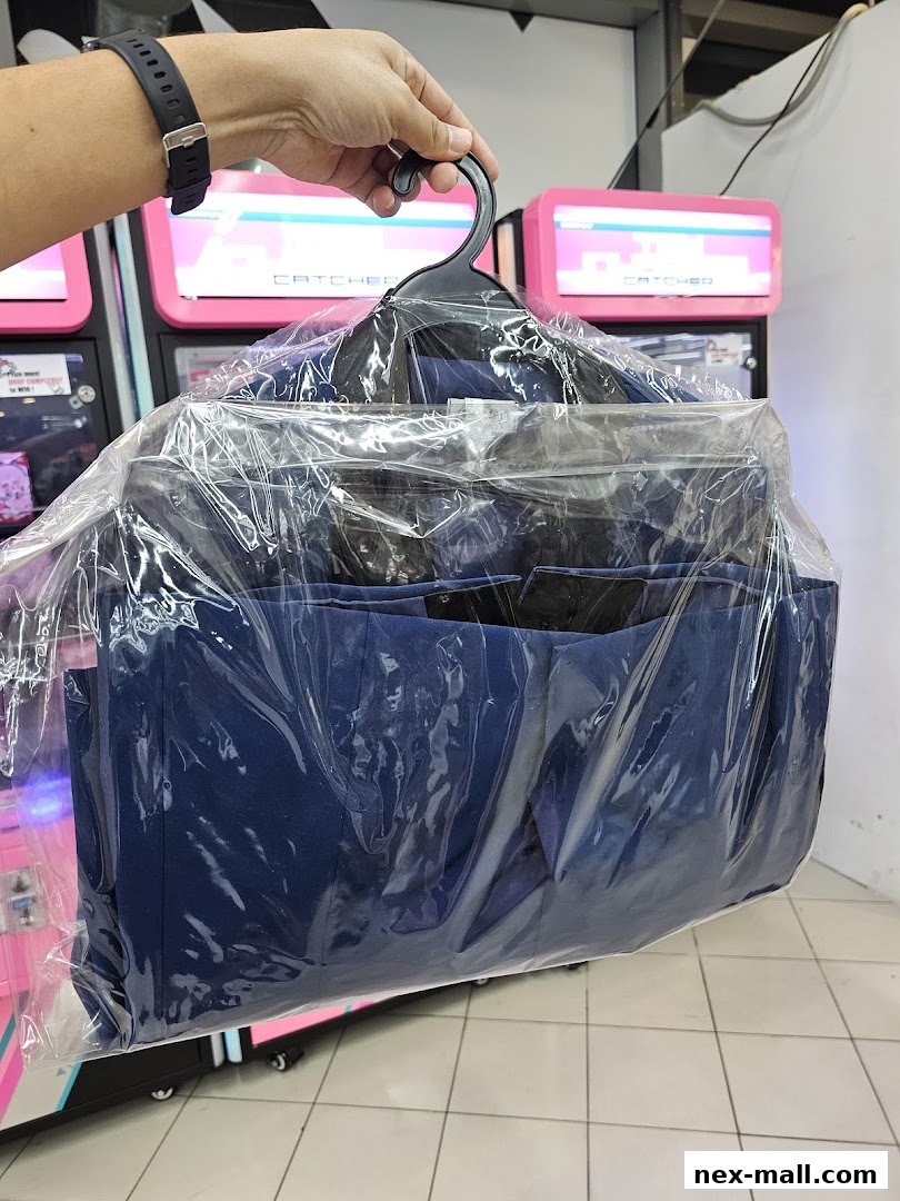 A hand holds a hanger with a blue suit, neatly packaged in plastic.