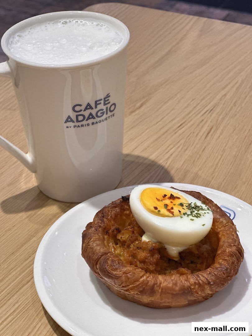 A savory pastry with a boiled egg on top, next to a mug of frothy coffee.