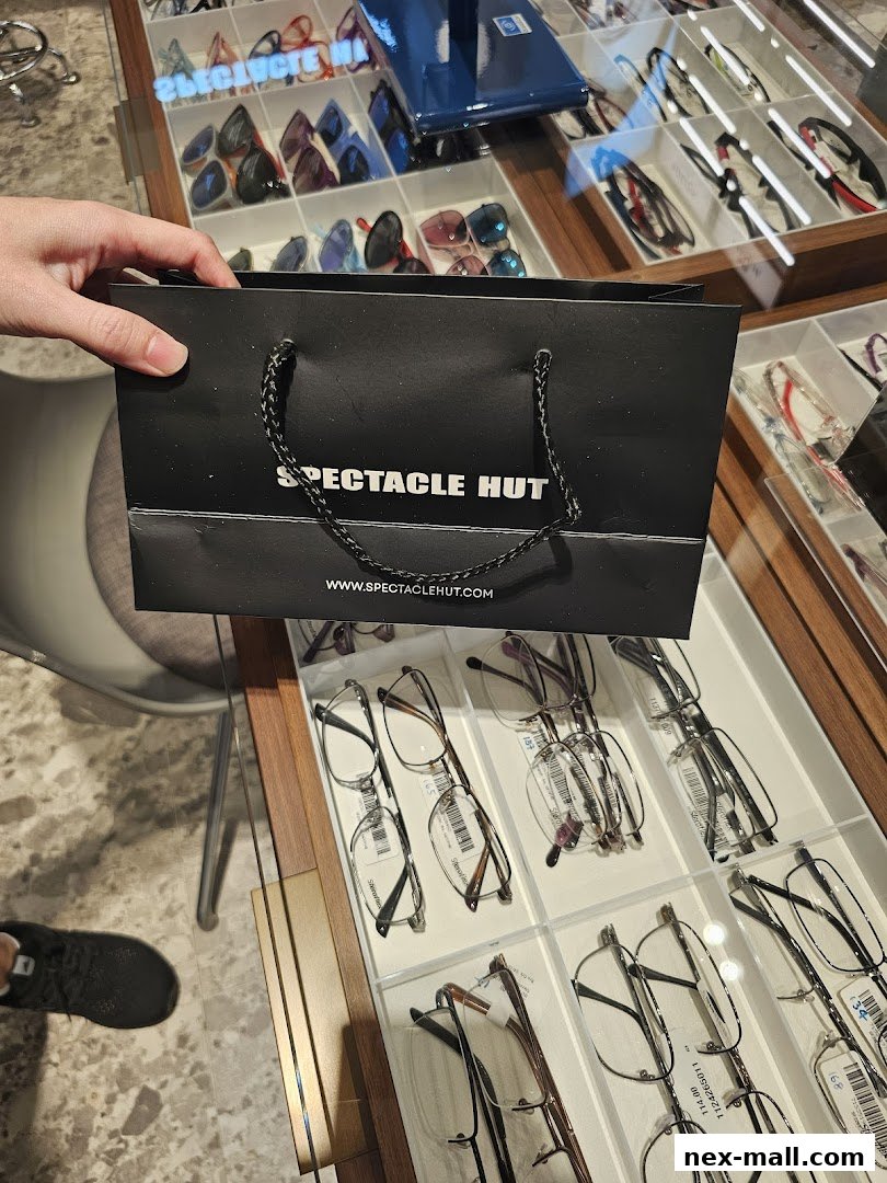 A person holds a Spectacle Hut shopping bag in front of a display of eyeglasses.