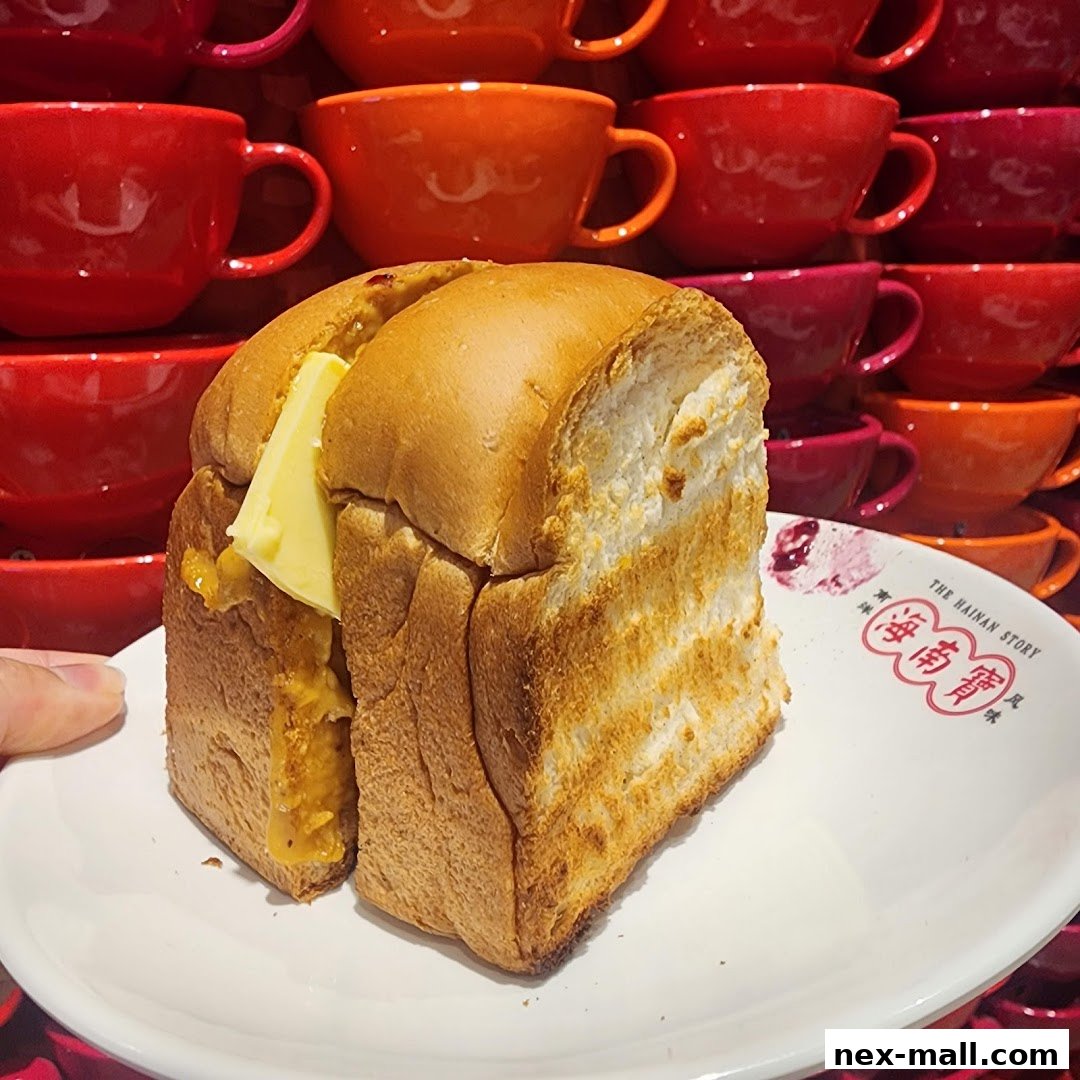 A close-up of a thick slice of kaya toast with butter on a white plate.