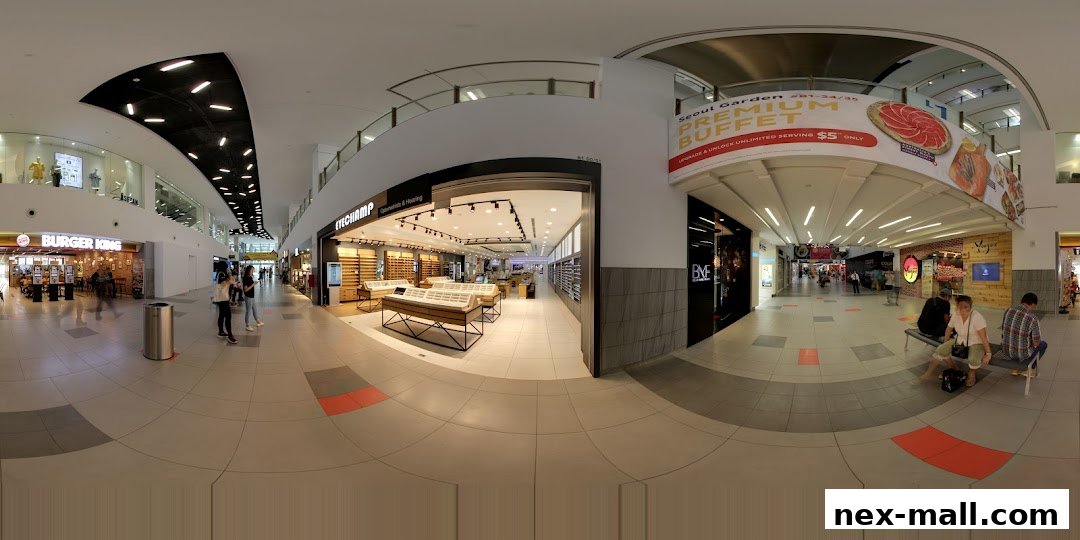 A wide-angle view of a shopping mall corridor with an optical shop and other stores.