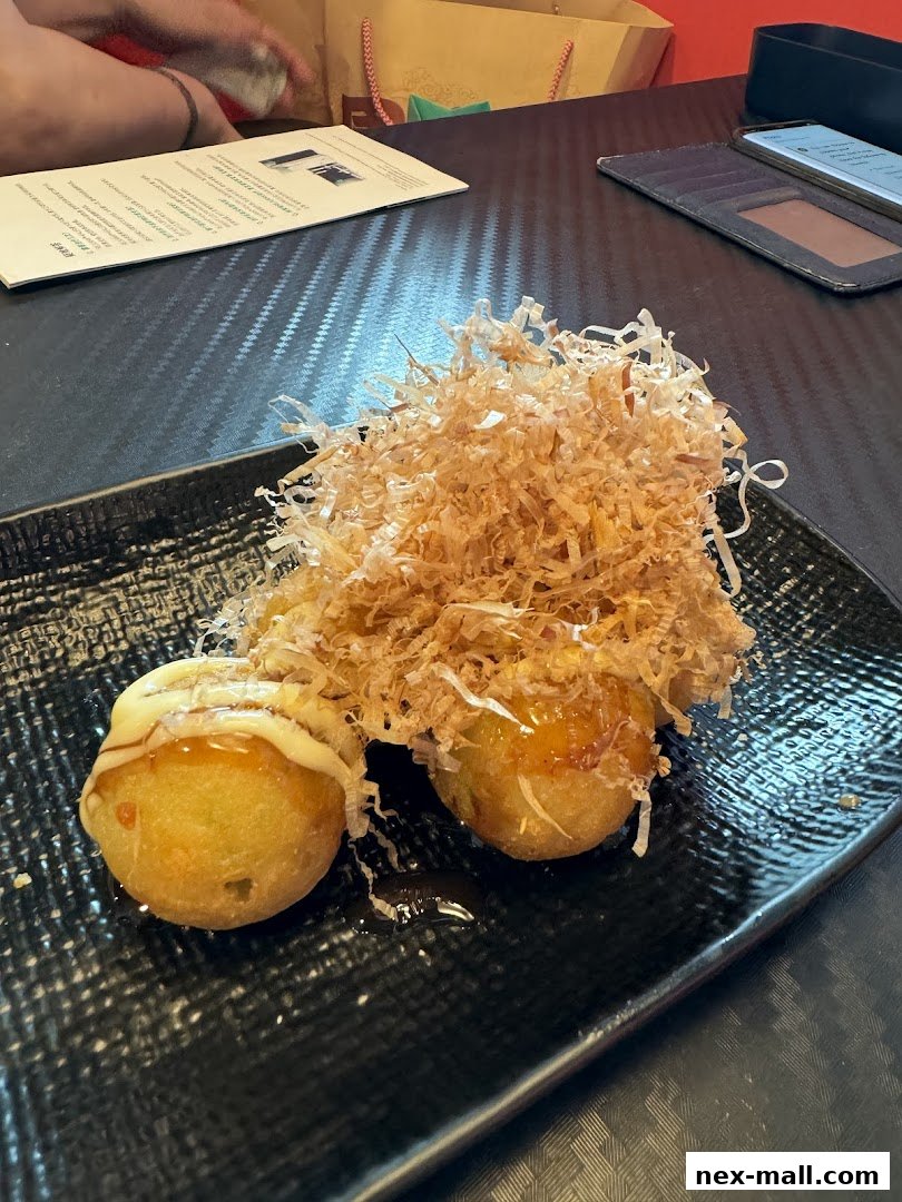 A plate of takoyaki topped with bonito flakes and sauce on a black plate.