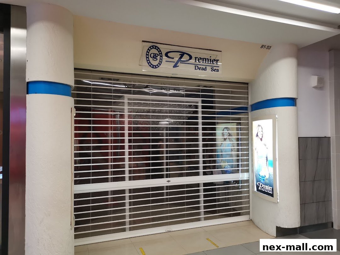 The closed storefront of Premier Dead Sea NEX, featuring a rolling security gate and promotional posters.
