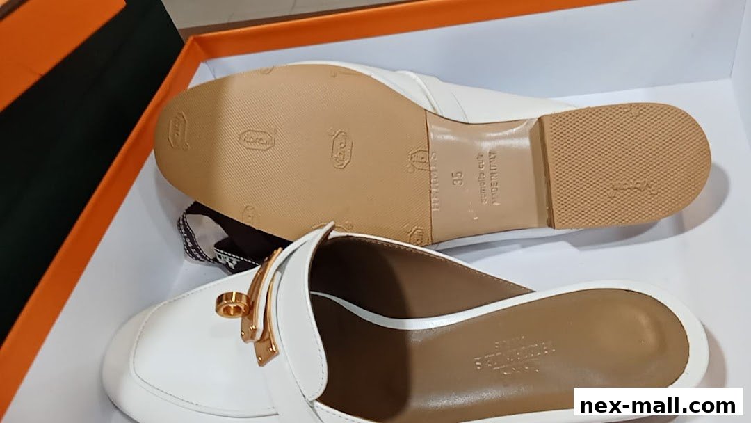 A pair of white leather mules with gold hardware, presented in a box.