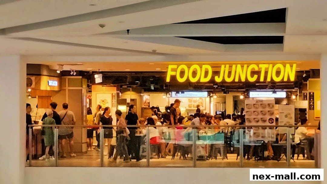 A busy food court with many people dining and queuing at various food stalls.