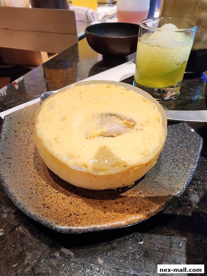 A close-up of a baked dish with a creamy topping, served on a textured plate with a drink in the background.