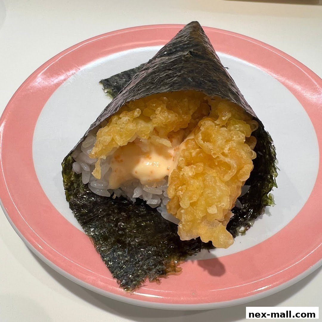 A close-up of a crispy tempura sushi hand roll with creamy sauce on a pink-rimmed plate.