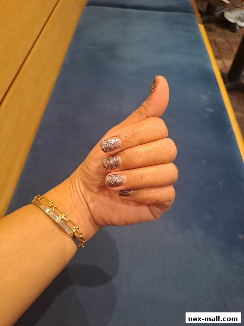 A hand with glittery nails gives a thumbs up, wearing a stylish bracelet.