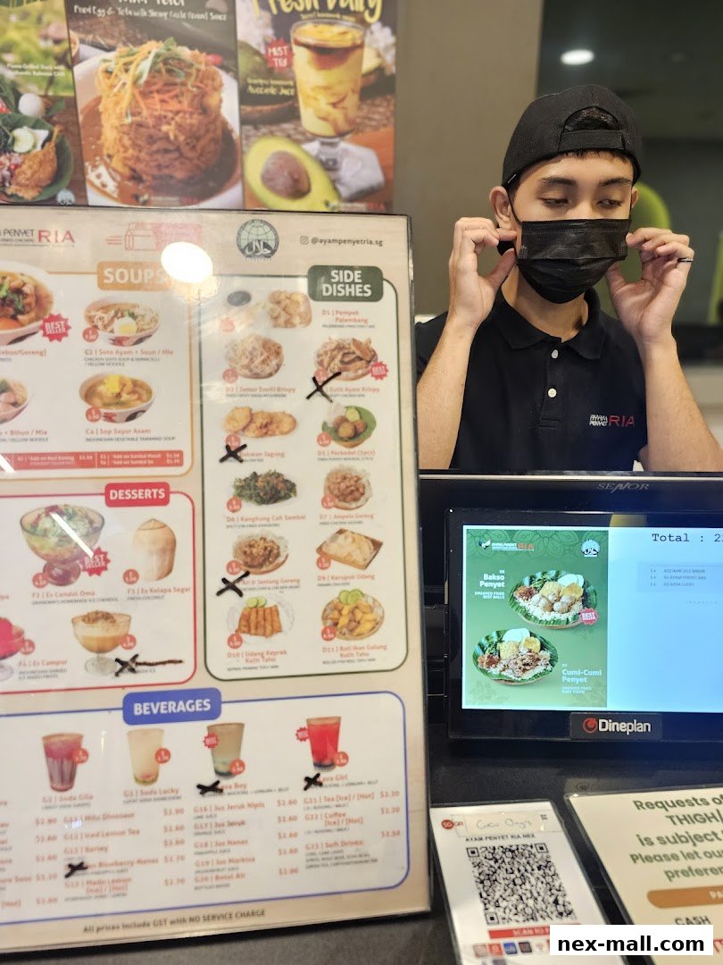 A menu for Ayam Penyet Ria with various dishes and beverages, and a staff member adjusting their mask.