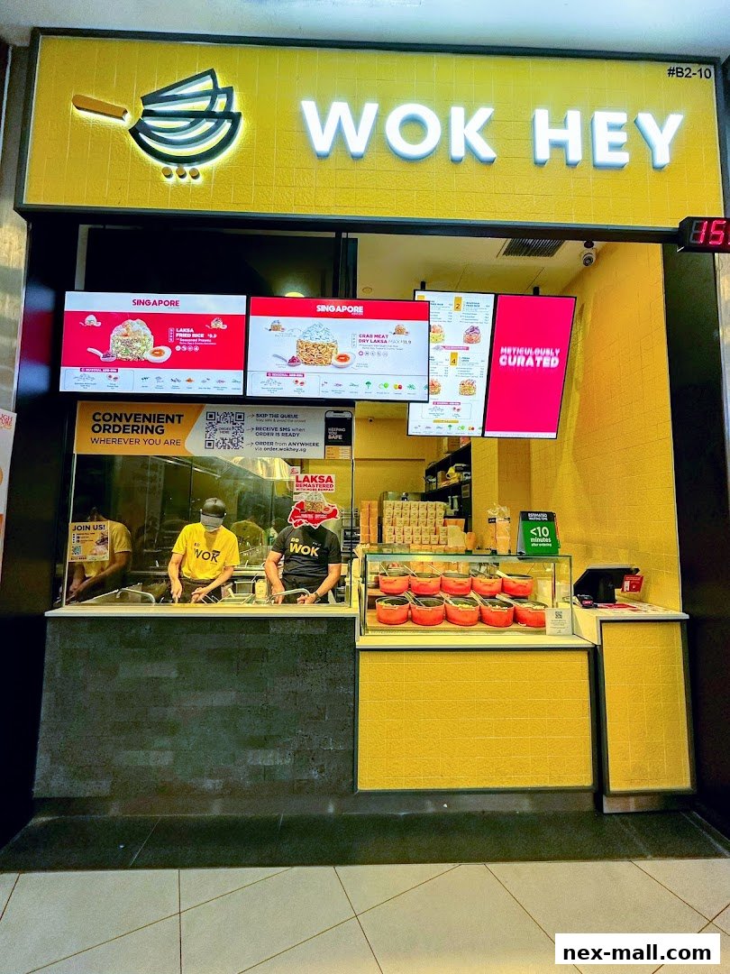 The Wok Hey NEX shop front with bright yellow accents and digital menu boards displaying food items.