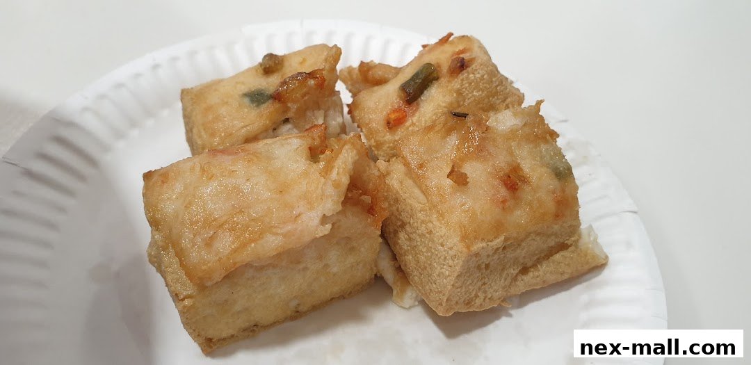 Close-up of fried tofu cubes with visible vegetables on a white paper plate.