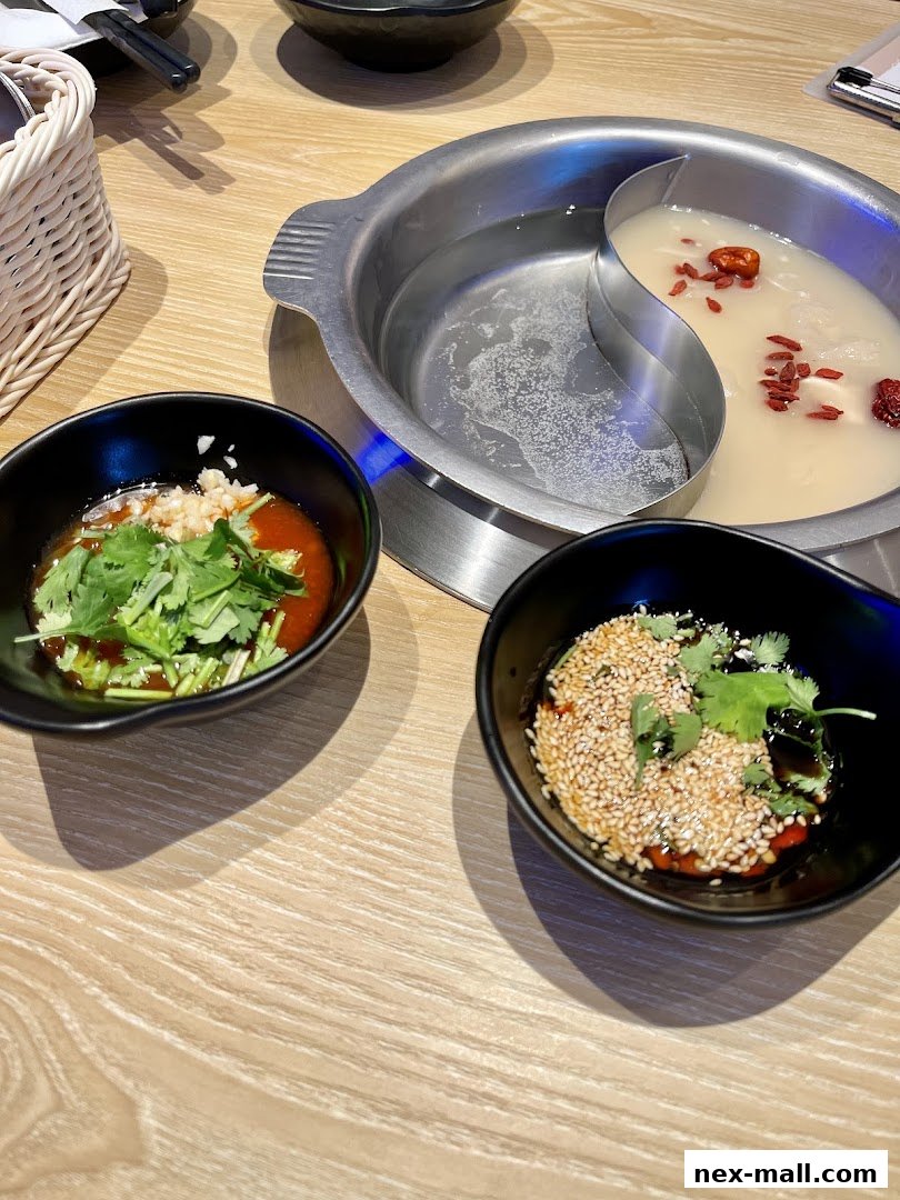 A split hot pot with two broths, served with dipping sauces and chopsticks.