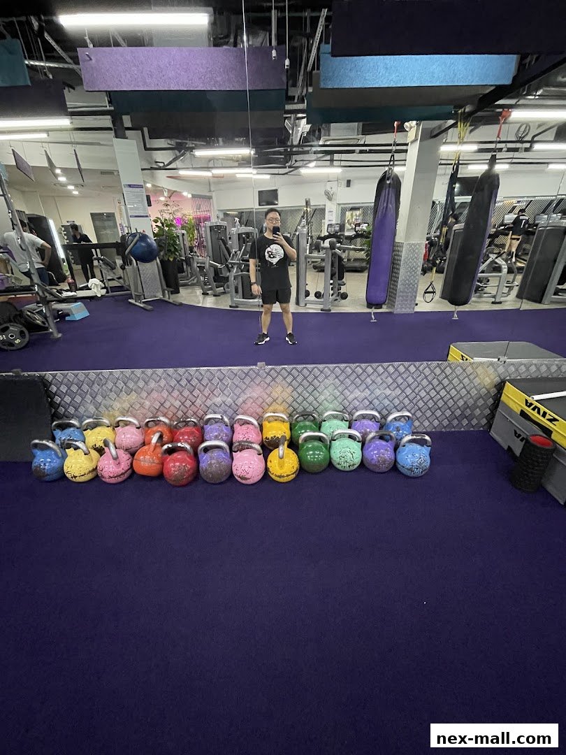 A person takes a mirror selfie in a gym with various exercise equipment and colorful kettlebells.