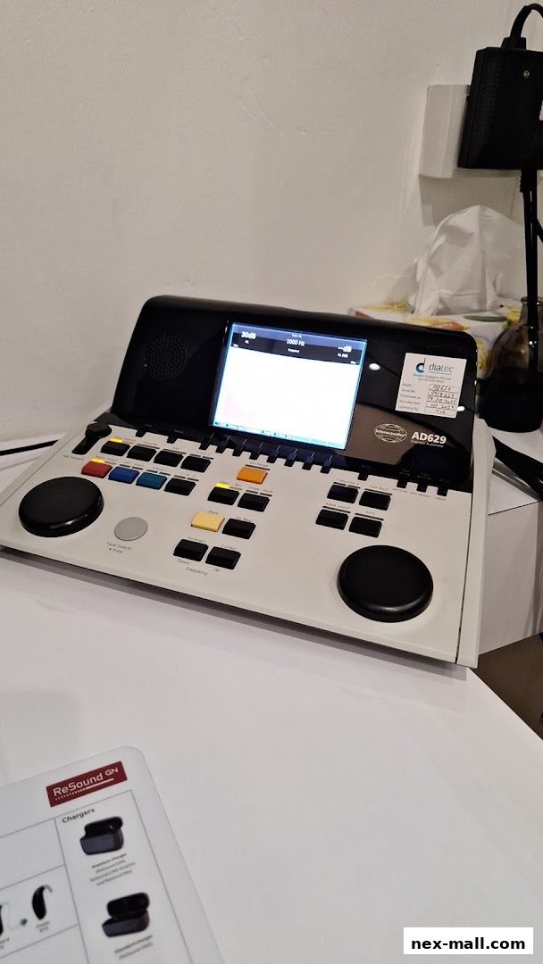 A hearing aid testing device with a screen and numerous buttons, along with product information.
