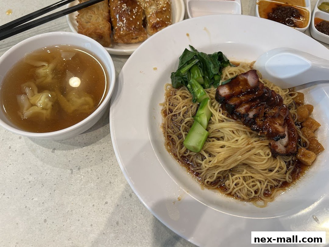 A close-up of a delicious bowl of wonton noodles with char siu and a side of wonton soup.