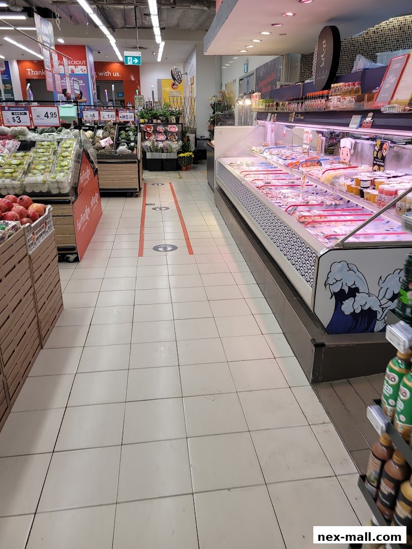 A wide aisle in a supermarket with fresh produce and a chilled display case.