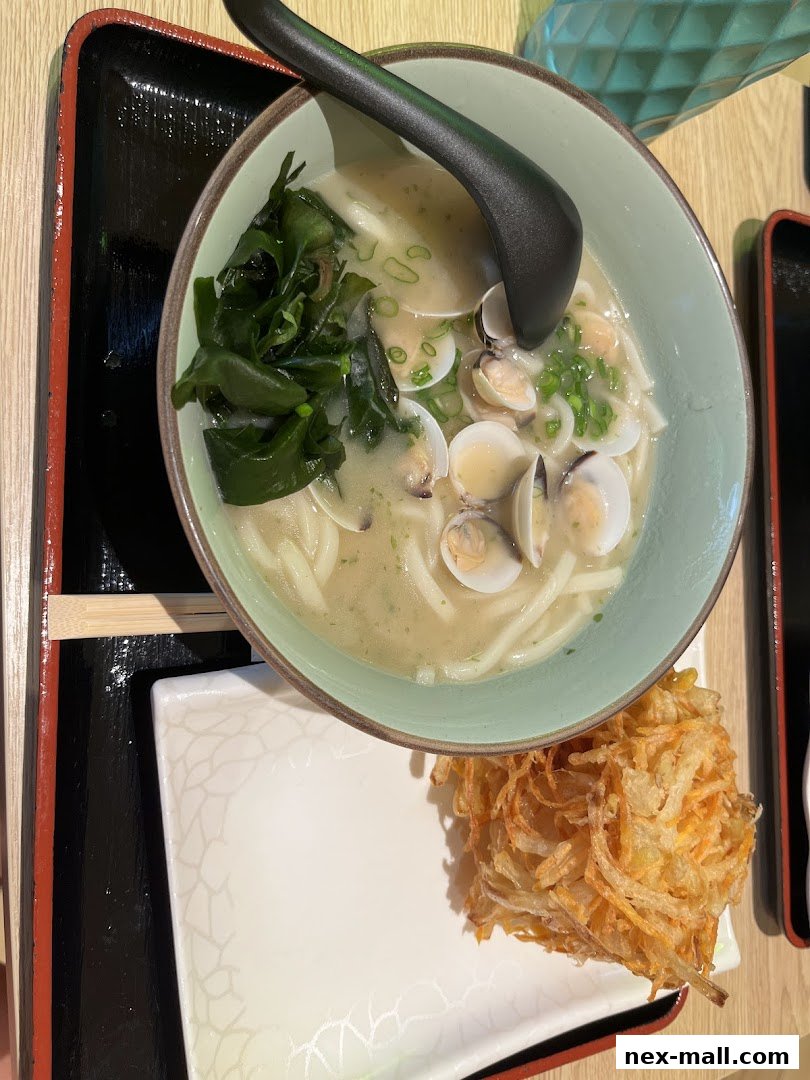 A bowl of Japanese udon soup with clams and seaweed, served with a side of tempura.