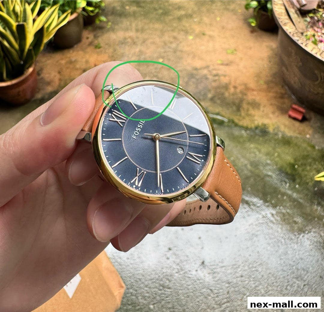 A hand holds a Fossil watch with a blue dial and brown leather strap.