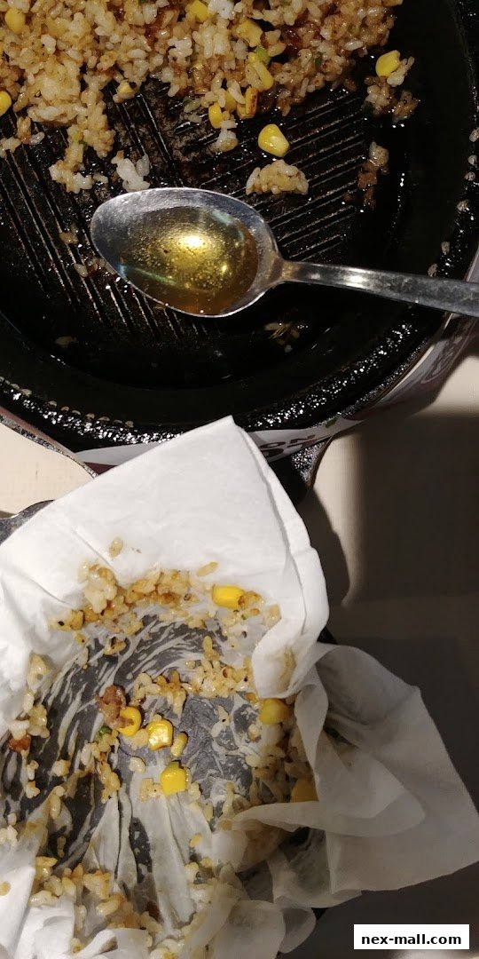 A close-up of a sizzling plate with rice, corn, and a spoon with oil.