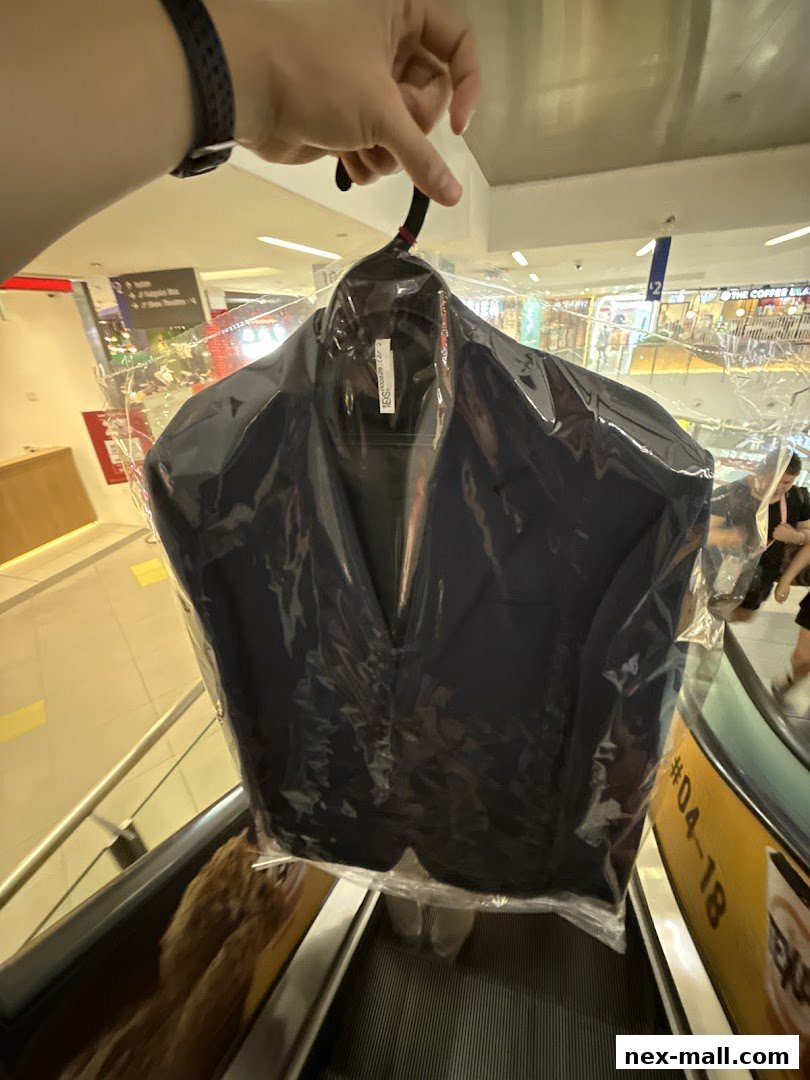 A person holds a freshly dry-cleaned navy blue blazer on a hanger.
