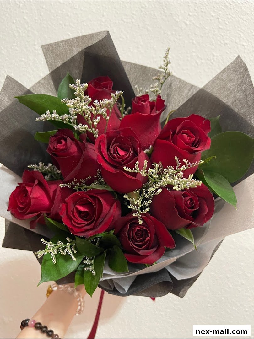 A hand holding a bouquet of deep red roses with delicate white filler flowers and green leaves.