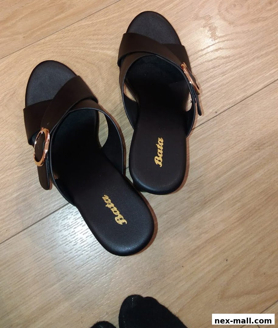 A pair of black Bata slide sandals with gold buckle detail on a wooden floor.