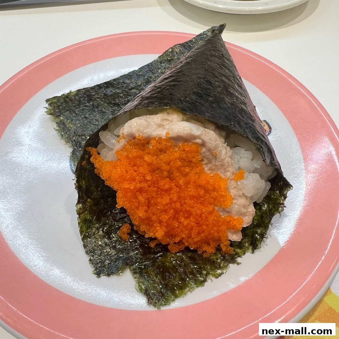 A close-up of a tuna temaki sushi roll with tobiko on a pink-rimmed plate.