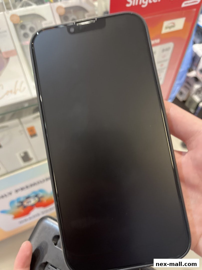 A hand holds a dark smartphone with a blank screen, showcasing phone accessories in the background.