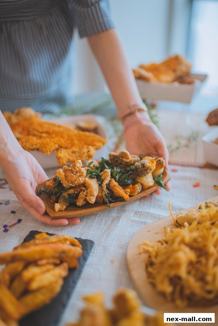 A person is serving a platter of fried chicken and other snacks on a table.