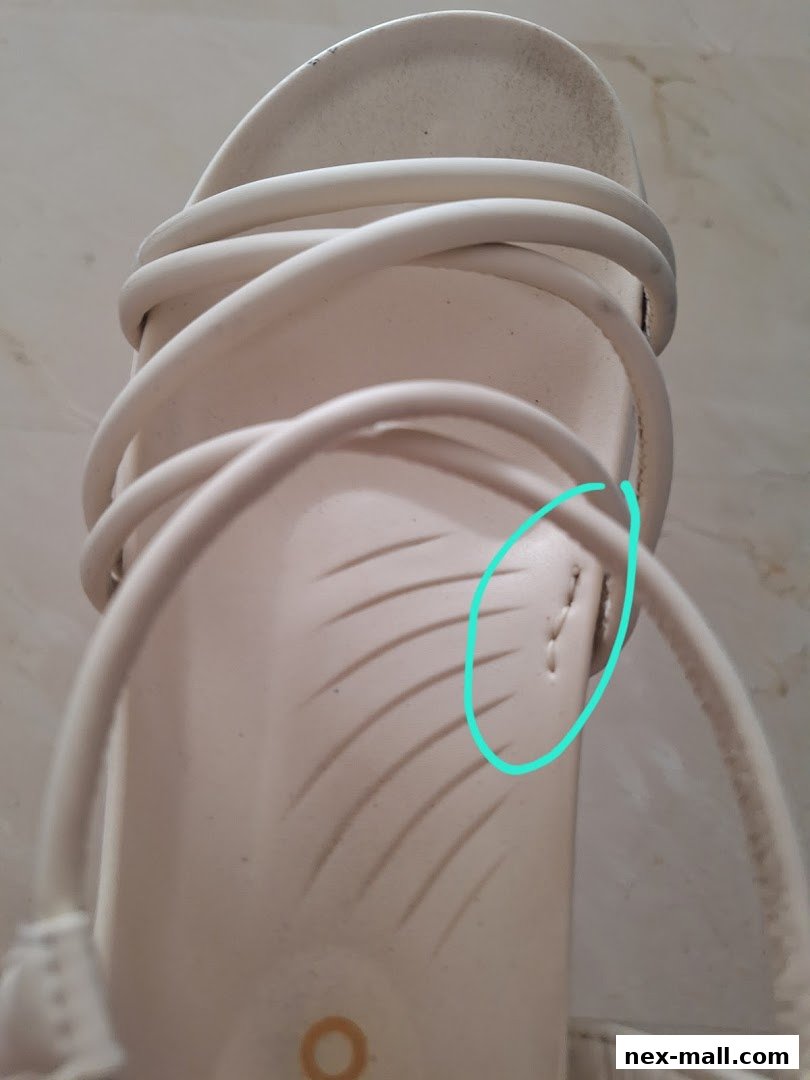 Close-up of a beige sandal with white straps and textured sole.