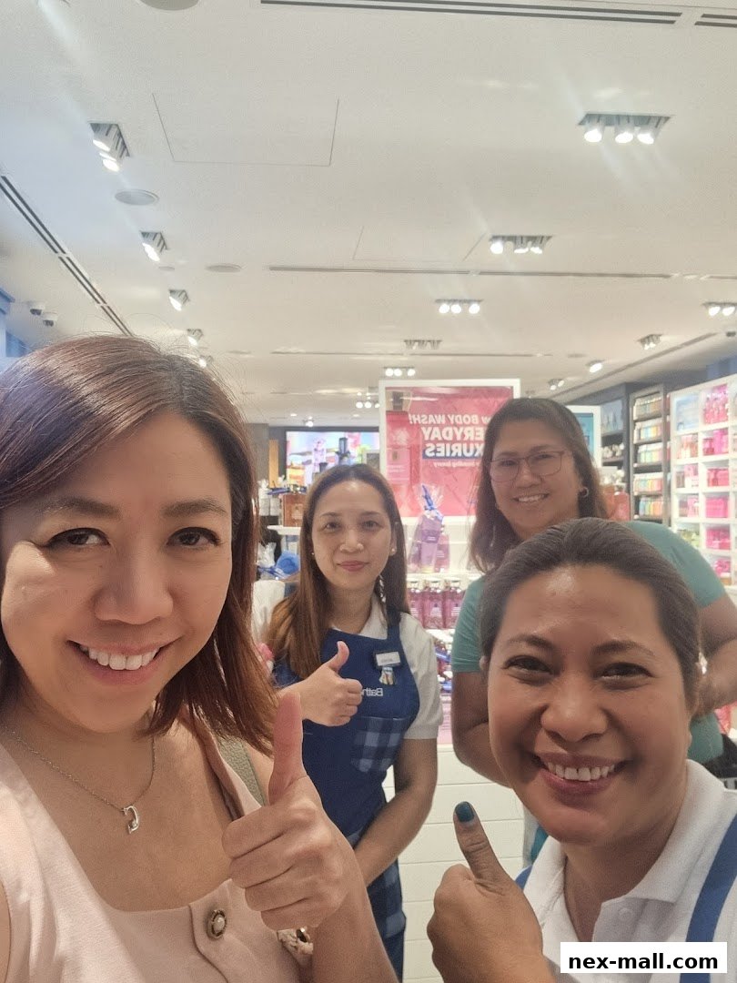 Four smiling women give thumbs up inside a brightly lit Bath & Body Works store.