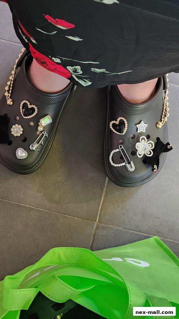A pair of black Crocs adorned with various charms, including hearts, stars, and safety pins.
