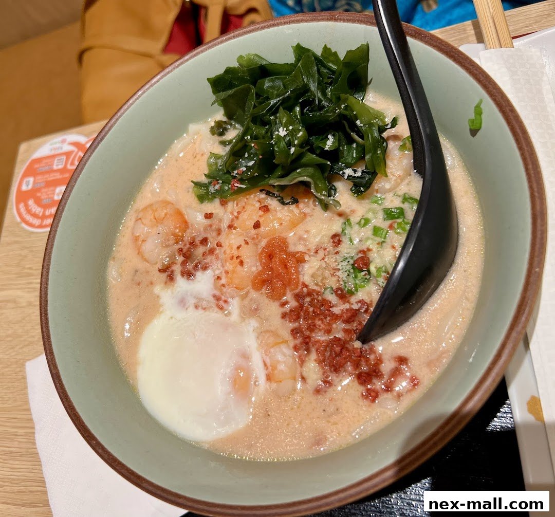 A close-up of a creamy udon noodle soup with shrimp, seaweed, and a poached egg.