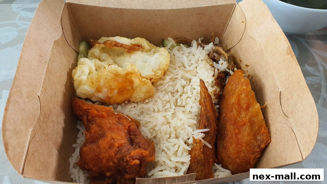 A takeaway box filled with nasi lemak, featuring rice, fried chicken, and a fried egg.