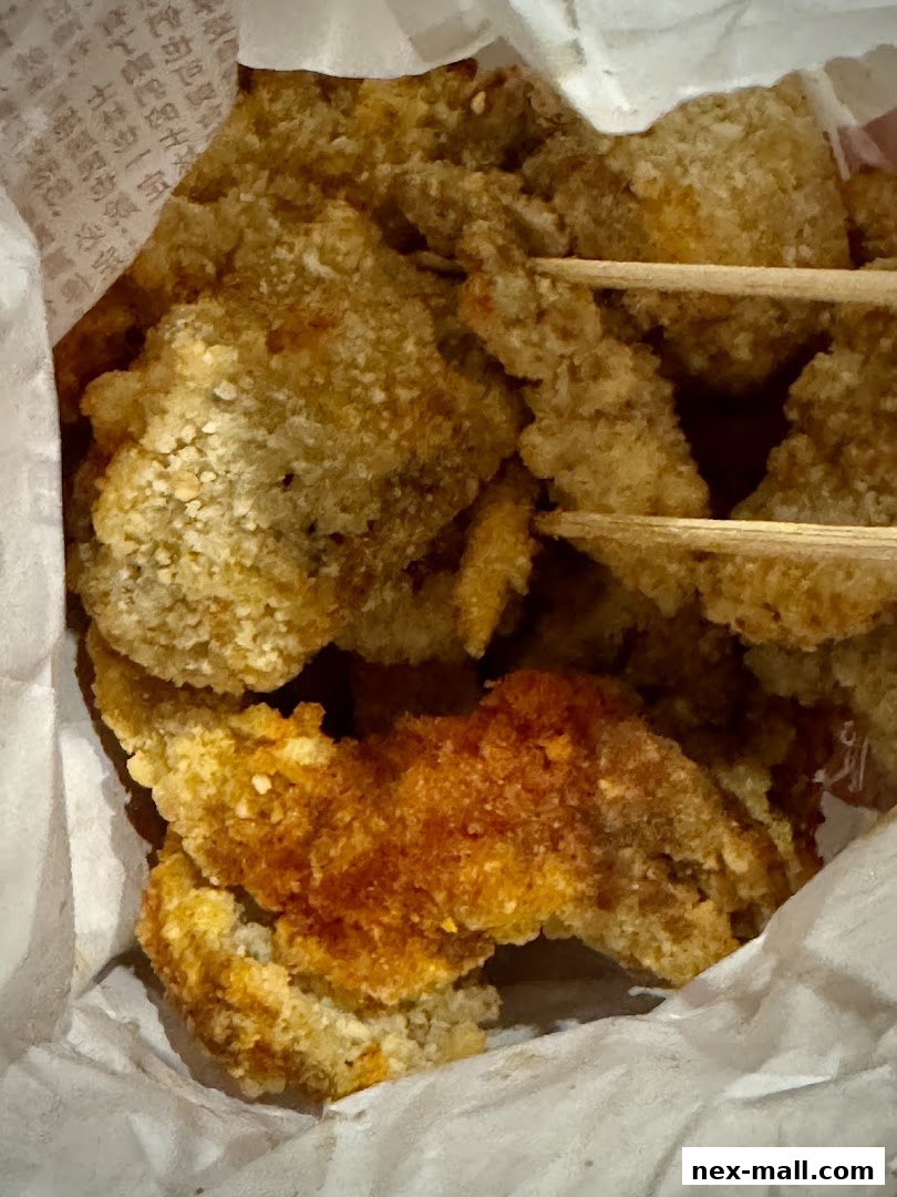 A close-up shot of crispy fried chicken pieces in a paper bag with chopsticks.