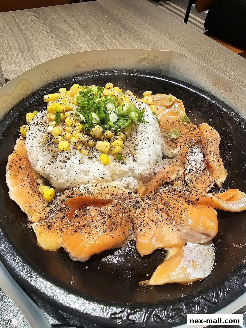 A sizzling hot plate of salmon, rice, and corn, seasoned with pepper and topped with green onions.