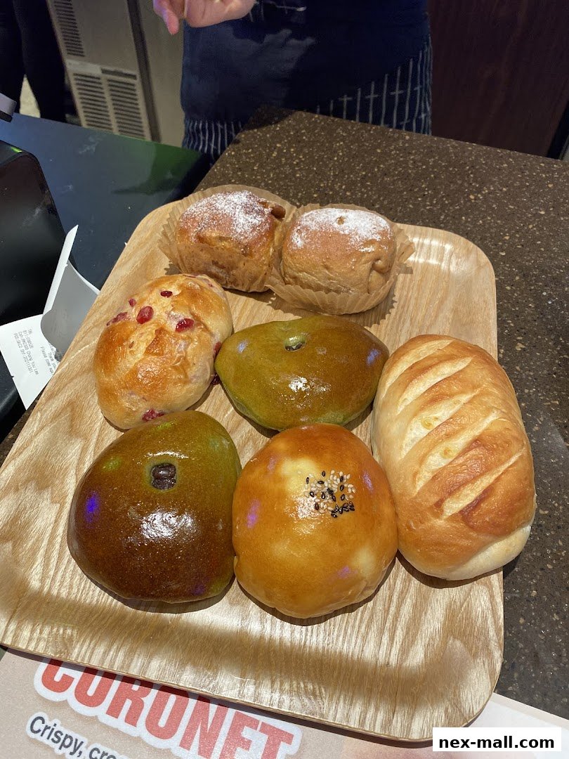 A wooden tray holds a variety of freshly baked Japanese pastries and breads.