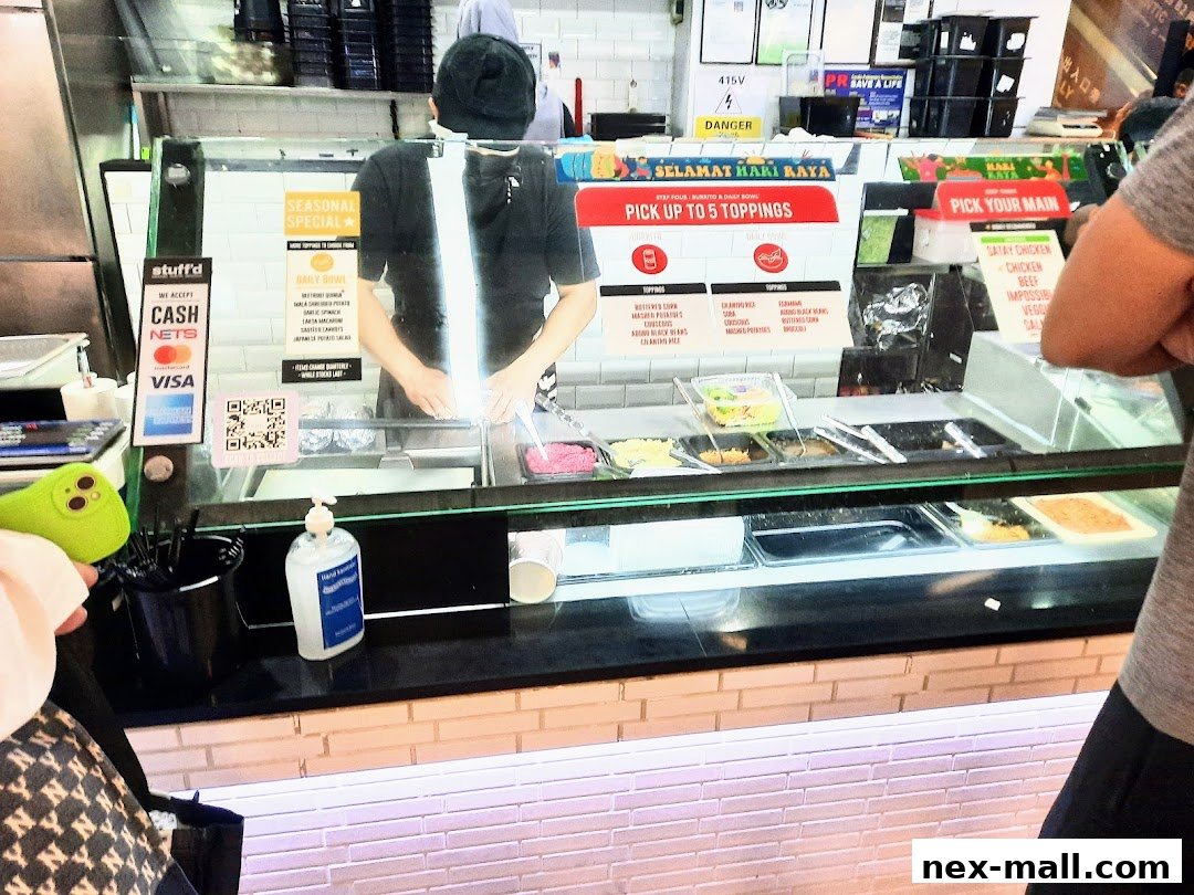 A food counter with various toppings and a staff member preparing a meal.