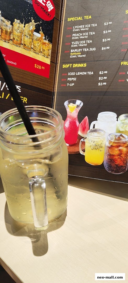 A close-up of a refreshing drink with a menu featuring teas and soft drinks in the background.