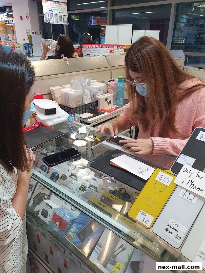 A shop assistant helps a customer at a counter displaying phone accessories and repair services.