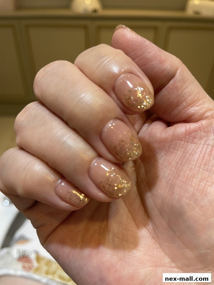A close-up shot of a hand with elegant nude nails adorned with gold glitter.