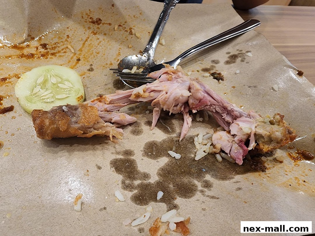 A close-up of leftover chicken bones, rice, and a cucumber slice on paper packaging.