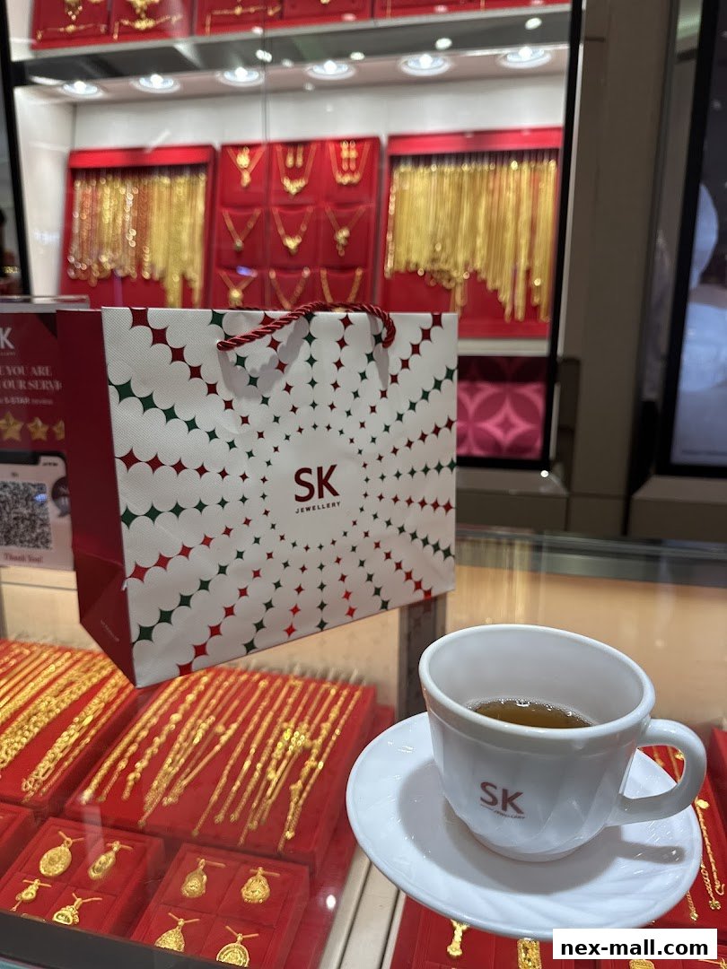 A shopping bag and a cup of tea sit on a counter in front of a display of gold jewelry.