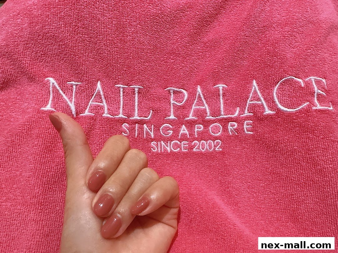 A hand with freshly painted nails rests against a pink towel with the Nail Palace logo.